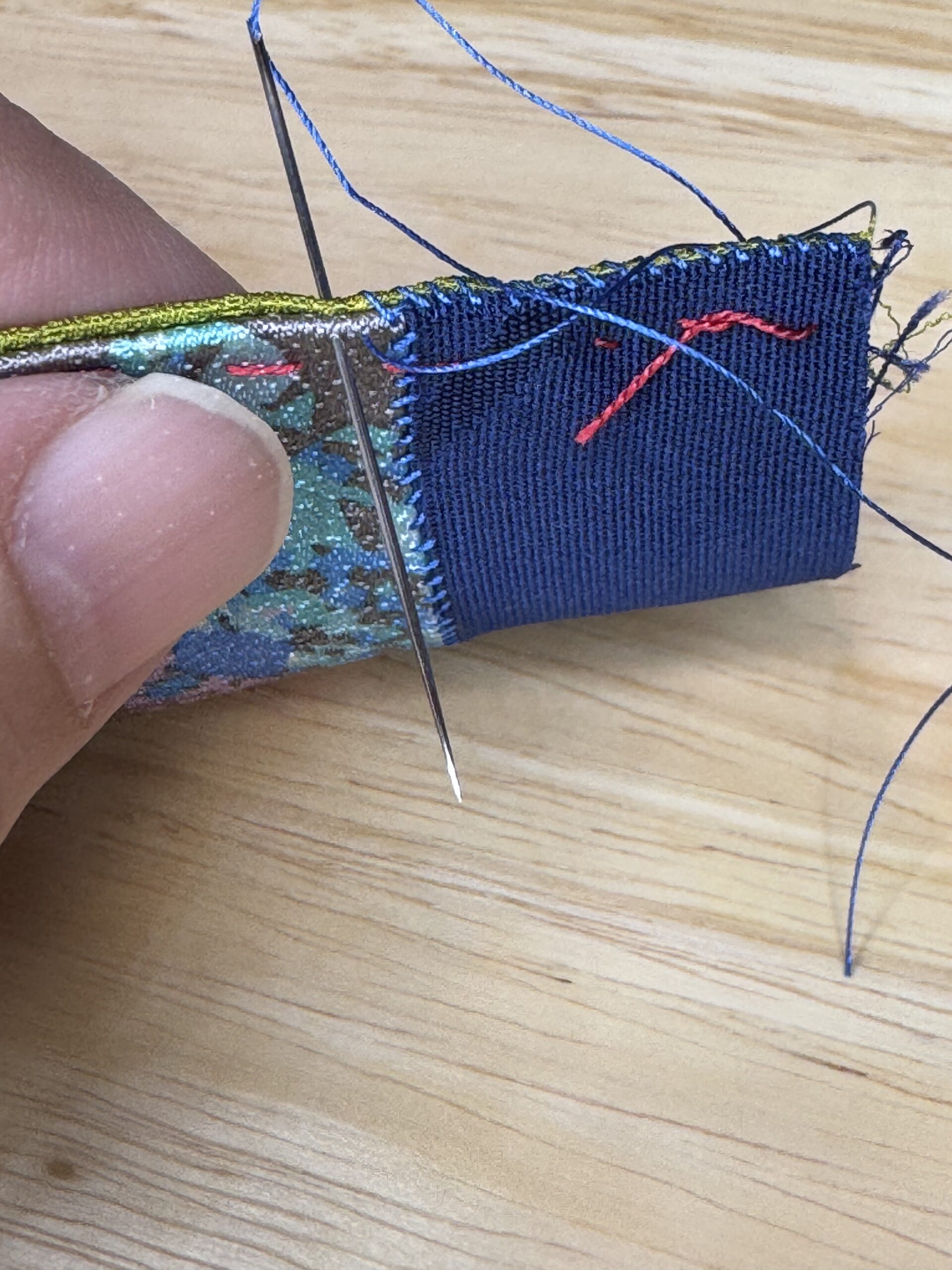 青や緑などの絹布を組み合わせた布を、針と糸で手縫いしているところ